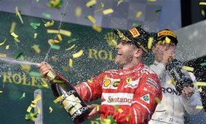 El piloto alemán de Ferrari, Sebastian Vettel, lanza champán mientras a su alrededor cae confetti para celebrar su victoria en el Gran Premio de Australia de Fórmula Uno, en Melbourne, Australia, el 26 de marzo de 2017. A su derecha está el piloto de Mercedes Valtteri Bottas, que terminó tercero. (AP Foto/Andy Brownbill)