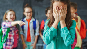 Schoolgirl crying on background of classmates teasing her